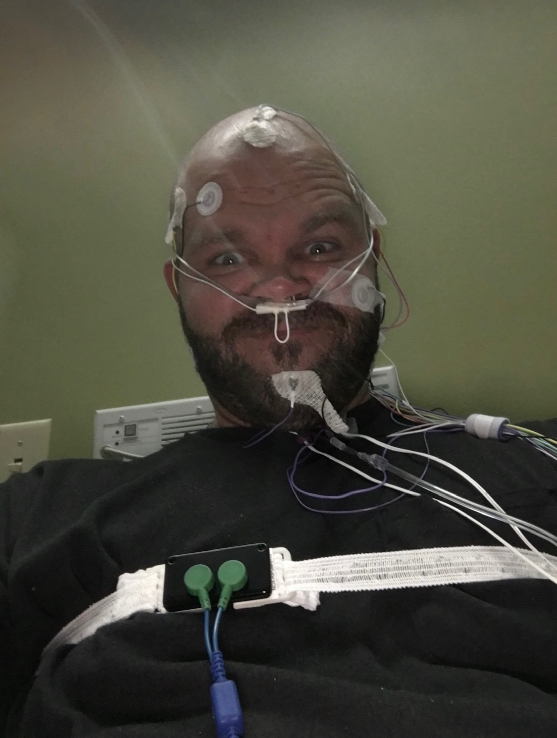Nick wired up with EEG electrodes, EKG leads, and a nasal cannula during a sleep / quantified-self study — self-experimentation as a methodology, not a lifestyle brand.