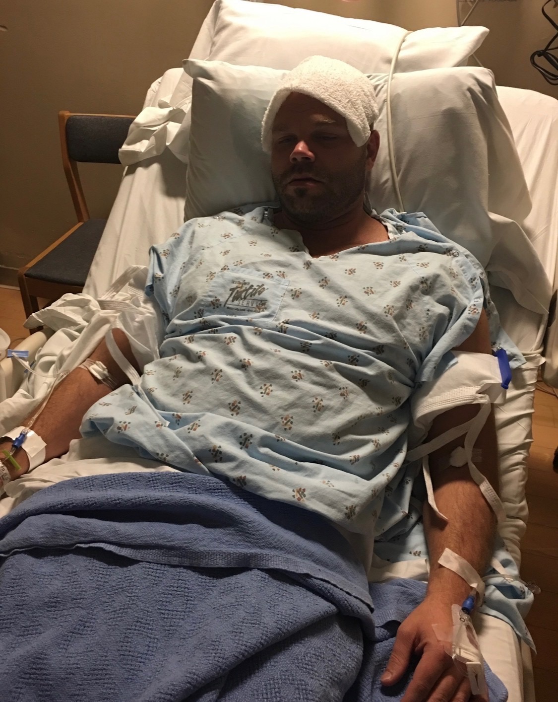 Nick in a hospital bed after the cardiac event — the moment the four lenses became one cross-disciplinary lens.